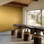 Rustieke eetruimte met een organisch gevormde houten tafel, boomstamkrukken en geel Arte-Terra Carvato 23924-behang op de achterwand.