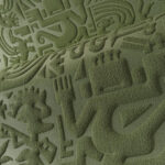 Detailopname van een groen reliëfoppervlak met Chimu-geïnspireerde figuren en symbolen uit de Arte-Terra collectie.