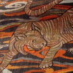Detail van het Arte Tigris behang uit de Gitane-collectie met een gestileerde tijger in warme aardetinten en abstracte achtergrond.