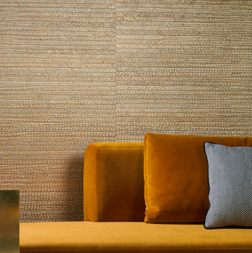 Detail van een woonkamer met Arte Twill behang 40330, een okergele fluwelen bank en een grijs sierkussen.