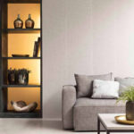 Moderne woonkamer met Arte Uno behang, grijze bank en sfeervol verlichte open kast met decoratieobjecten.