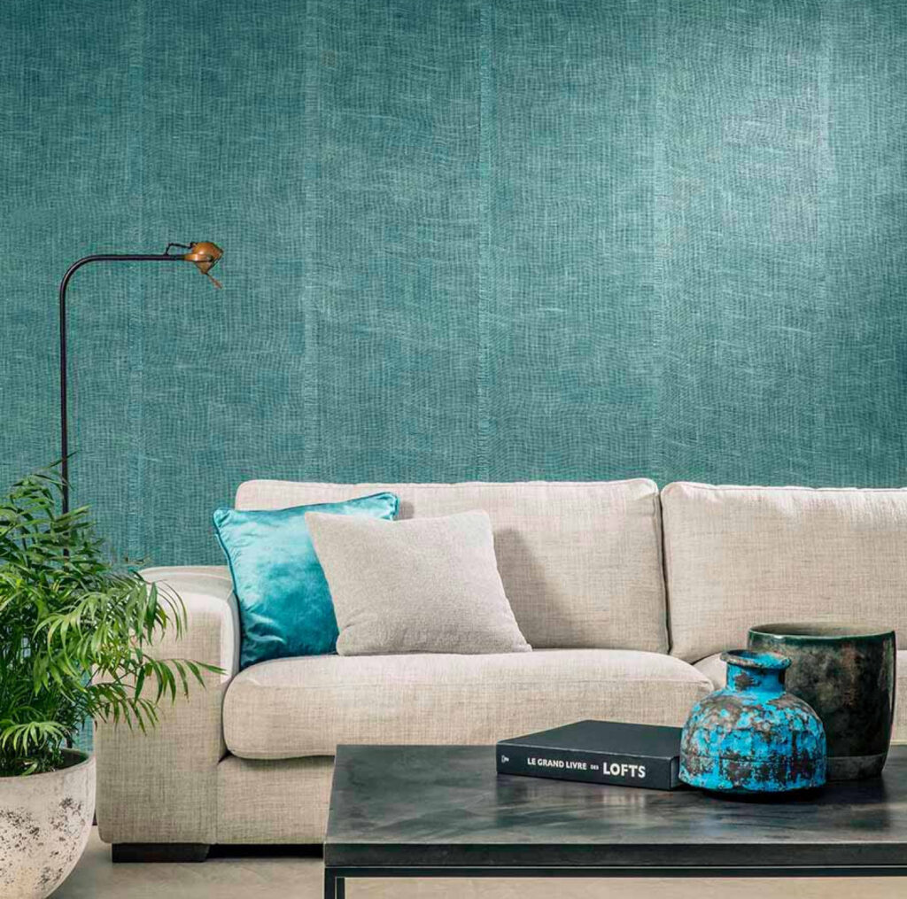 Moderne woonkamer met lichtbeige bank, turquoise Arte Uno behang en decoratieve accessoires op een salontafel.