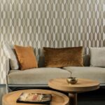 Zithoek met beige bank, bruine kussens en Arte-behang Arrow met geometrisch patroon op de achtergrond.