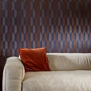 Lichtbeige bank met roestkleurig kussen voor een muur met Arte-behang Arrow 2 in donkerblauw en bruin geometrisch patroon.