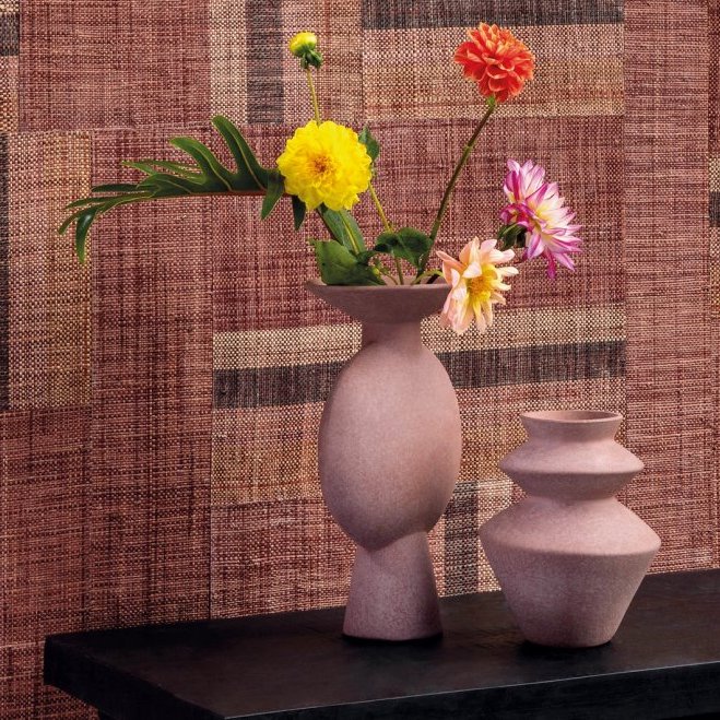 Twee roze keramische vazen met bloemen staan voor een roodbruin Arte Atelier Boro behang met textuurpatroon.