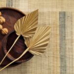 Twee gedroogde palmbladeren en walnoten in een houten schaal op Arte-behang Atelier Boro AT73.