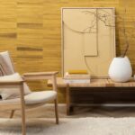 Interieurhoek met Arte-behang uit de Atelier Naturally Beautiful AT-24 collectie, een houten stoel, kunstwerk, boeken en een witte vaas met takken op een bankje.