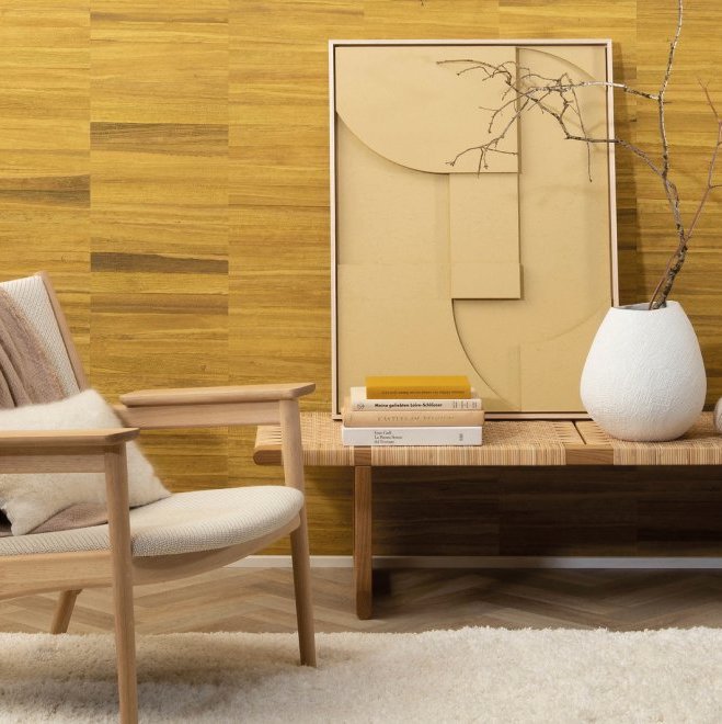 Interieurhoek met Arte-behang uit de Atelier Naturally Beautiful AT-24 collectie, een houten stoel, kunstwerk, boeken en een witte vaas met takken op een bankje.