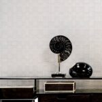 Moderne interieursetting met Arte behang Avalon Weave als achtergrond en decoratieve objecten op een glazen tafel.