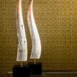 Twee sculpturen op sokkels voor een gouden Arte-behang met Avalon Weave-patroon.
