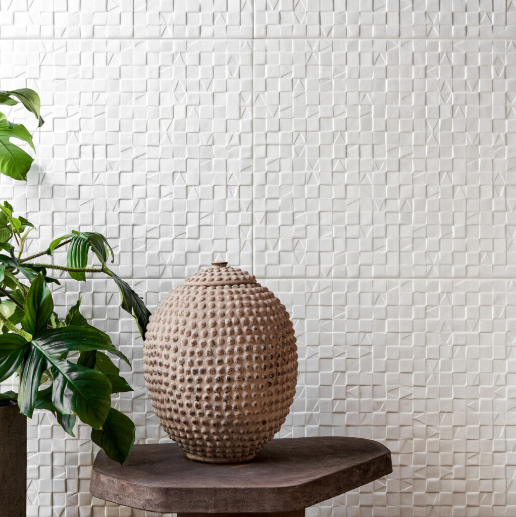 Decoratieve ruimte met Arte behang Babylon in reliëfpatroon, een aardewerken pot en groene plant op een houten tafel.