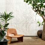 Moderne interieursetting met houten stoel, tropische planten en wit reliëfbehang uit de Arte Babylon Between Rivers-collectie met jungletafereel.