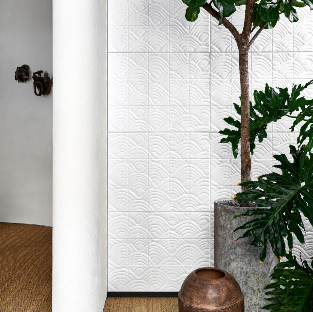 Witte wand met reliëfbehang Arte Babylon Terracotta 97010, omringd door groene planten en aardetinten.