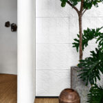 Witte wand met reliëfbehang Arte Babylon Terracotta 97010, omringd door groene planten en aardetinten.
