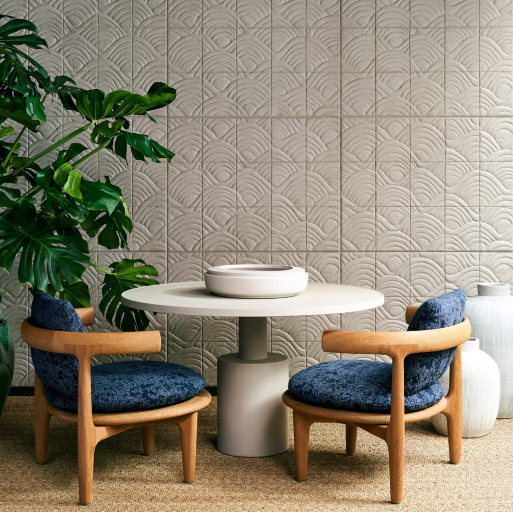 Moderne zithoek met houten stoelen en ronde tafel tegen een Arte Babylon Terracotta 97012 behangwand met reliëfpatroon.