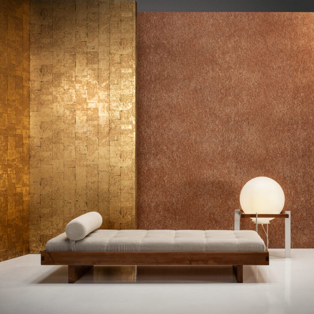 Moderne interieursetting met Arte Boutique Gilded Heritage 90500 behang in goud en koper, een houten ligbed en een ronde tafellamp.