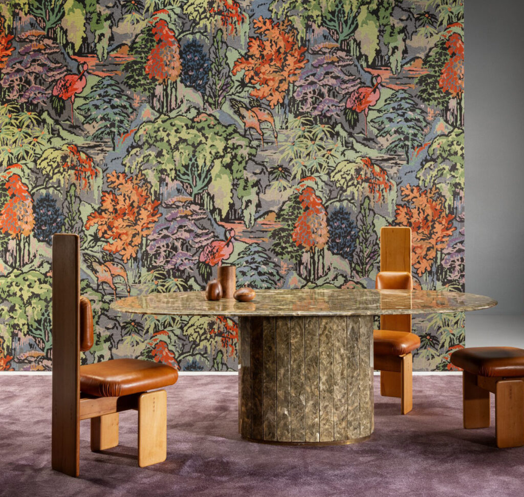 Sfeervolle interieursetting met Boutique Riverbank 90515 behang van Arte, een kleurrijk patroon met bomen en vogels, achter een ronde tafel en designstoelen.