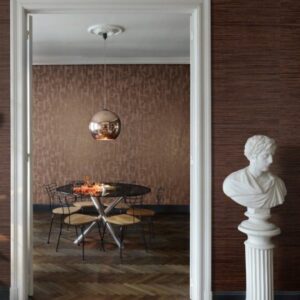 Luxe eetkamer met Arte Cobra CA5 behang, ronde tafel, koperen hanglamp en klassieke buste in de deuropening.