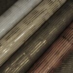 Vier rollen Arte Cobra CA5 behang met glanzende, houtnerfachtige textuur in grijs-, beige-, bruin- en koperkleuren.