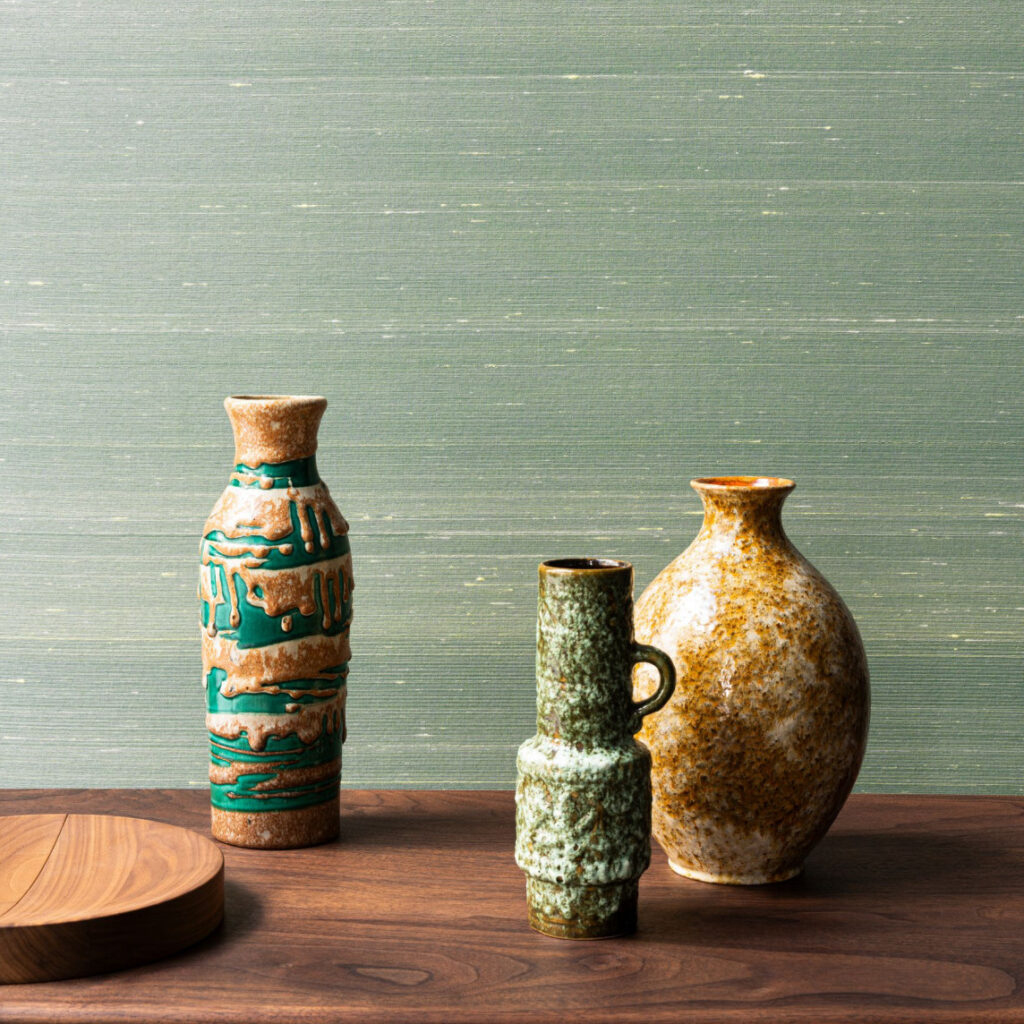 Keramische vazen en een houten schaal op een houten tafel tegen groen Arte Dupion behang.