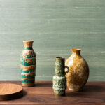 Keramische vazen en een houten schaal op een houten tafel tegen groen Arte Dupion behang.