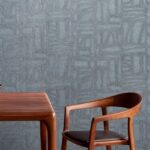 Houten tafel en stoel voor een blauwe muur met Arte Essentials Costura Bojagi 57543 behang.