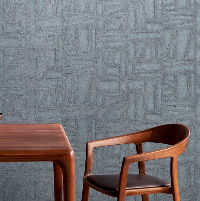 Houten tafel en stoel voor een blauwe muur met Arte Essentials Costura Bojagi 57543 behang.