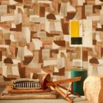 Interieur met Arte Essentials Costura Urban 57601 behang in aardetinten, houten meubelen en een moderne lamp.