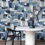 Ronde witte tafel met zwarte stoel en blauwe vaas voor een muur met geometrisch Arte Essentials Costura Urban 57604 behang in blauwtinten.