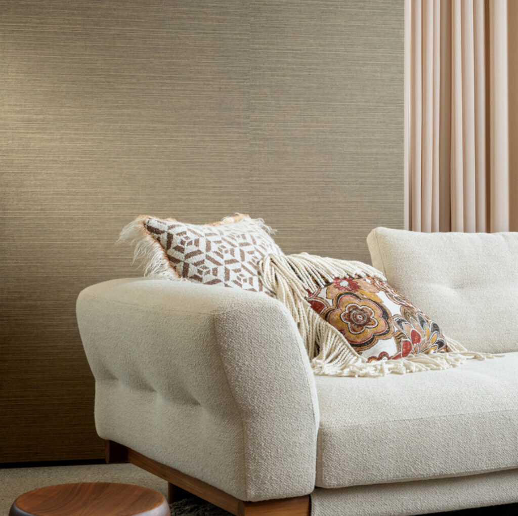 Beige bank met sierkussens voor een muur met Arte behang uit de Essentials Les Naturels Le Sisal collectie.