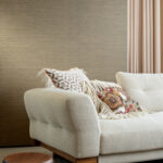 Beige bank met sierkussens voor een muur met Arte behang uit de Essentials Les Naturels Le Sisal collectie.