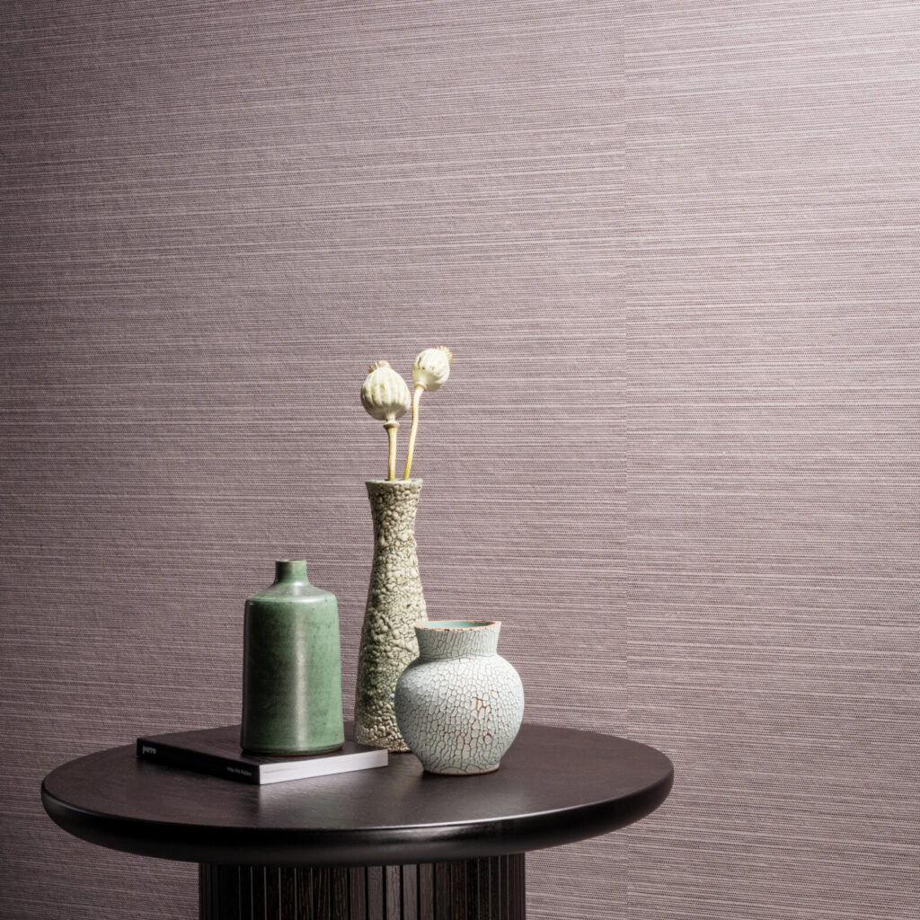 Stijlvolle opstelling met keramische vazen op een ronde tafel tegen Arte-behang Essentials Les Naturels Le Sisal 26708 in een zachte, geweven textuur.