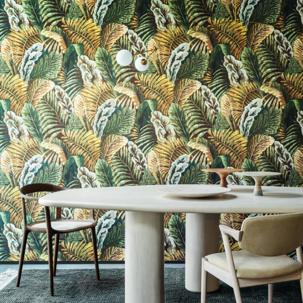 Moderne eetkamer met een rond tafelblad en stoelen, tegen een opvallende tropisch gebladerd Arte-behang uit de Essentials Les Naturels collectie (Verdure 26760).