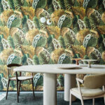 Moderne eetkamer met een rond tafelblad en stoelen, tegen een opvallende tropisch gebladerd Arte-behang uit de Essentials Les Naturels collectie (Verdure 26760).