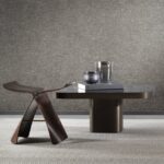 Moderne interieursetting met Arte-behang Essentials Les Nuances Chanderi, een sculpturale donkerbruine stoel en een lage tafel met decoratieve objecten.