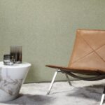 Designinterieur met Arte-behang Essentials Les Nuances Chanderi, een leren designstoel en een marmeren bijzettafel op een lichtgrijs vloerkleed.