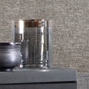 Glazen en keramische kom op een grijze ondergrond tegen een wand met Arte Essentials Les Nuances Chanderi behang.