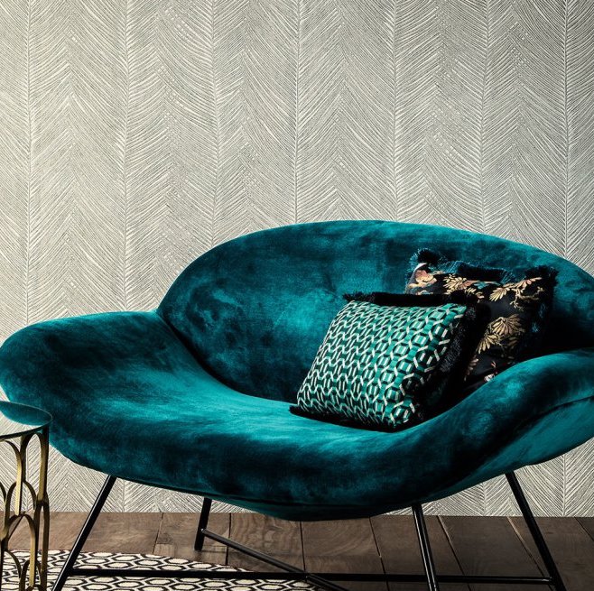 Fluwelen turquoise fauteuil met decoratieve kussens voor een muur met Arte-behang Essentials Talamanca in een subtiel patroon.