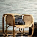 Rieten stoel met zwart sierkussen staat voor een muur bekleed met Arte behang uit de Essentials Travellers Horizon collectie.