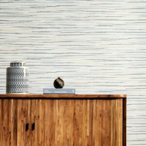 Houten kast met decoratieve objecten tegen een muur bekleed met Arte Essentials Travellers Horizon behang in een horizontaal gestreept patroon.
