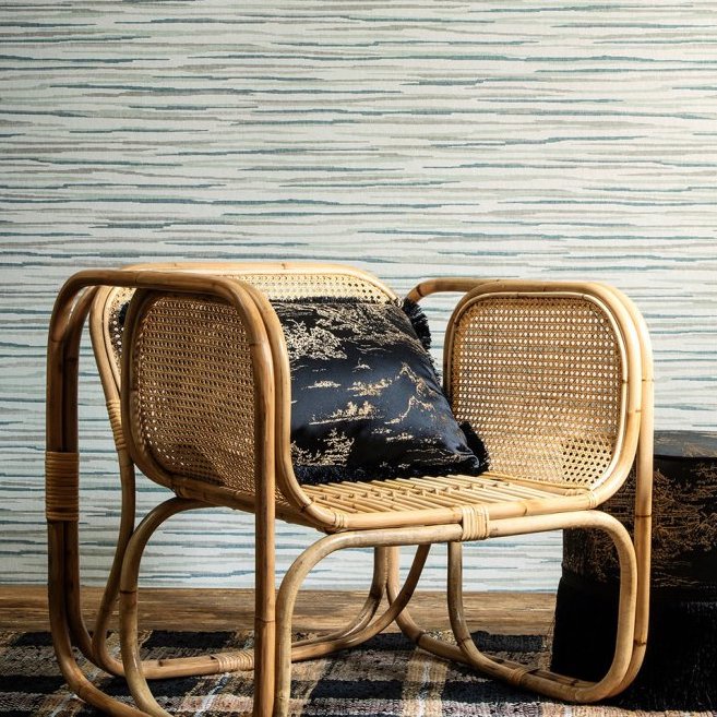 Rieten stoel met zwart sierkussen staat voor een muur bekleed met Arte behang uit de Essentials Travellers Horizon collectie.