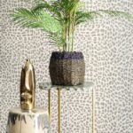 Vlechtmand met groene plant op een marmeren bijzettafel tegen Arte Essentials Travellers Pelage behang met panterprint.