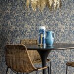 Eetkamer met rieten stoelen, blauwe keramiek en Arte Essentials Travellers Tantor behang met oosters motief op de achtergrond.