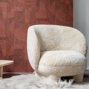 Crèmekleurige, zachte fauteuil op een harig vloerkleed voor een rode muur met Arte-behang Essentials Tangram Caprice Coral.