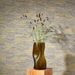 Bruine vaas met bloemen op houten sokkel voor geometrisch Arte-behang uit de Essentials Totem Infinity 18932 collectie.