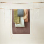 Stalen van Arte-behang uit de Essentials Washed Linen collectie in diverse natuurlijke kleuren hangen aan touwen.