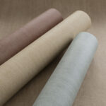 Drie rollen Arte Essentials Washed Linen behang in verschillende natuurlijke kleuren op een bijpassende ondergrond.