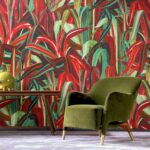 Groen fluwelen fauteuil en houten bijzettafel met lamp staan voor kleurrijk Arte-behang uit de Expedition Java-collectie met een tropisch bladerpatroon.