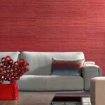 Moderne woonkamer met Arte-behang Expedition Tasar in roodtinten achter een lichtgrijze bank met sierkussen.