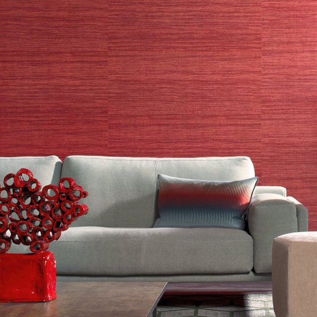 Moderne woonkamer met Arte-behang Expedition Tasar in roodtinten achter een lichtgrijze bank met sierkussen.
